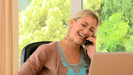 mujer joven riendo en el teléfono y trabajando en una computadora portátil