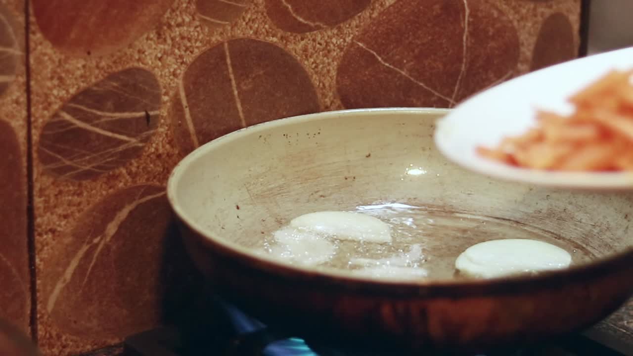 Adding white onions and carrots to a pan with hot oil to be lightly fried showing a candid moment of slow living and home cooking