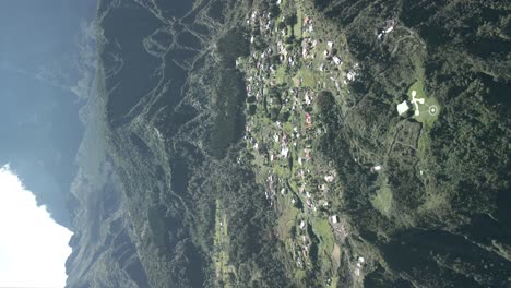 video vertical sin graduar de un dron que vuela hacia el cráter de un volcán gigante con casas y pequeños pueblos