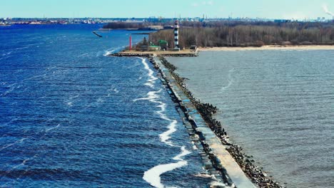 bolderāja mols in early spring: showcasing a distinct water color divide of deep blue and murky gray, with a lighthouse and waves, captured from an elevated perspective with a standard lens