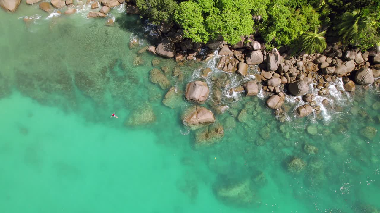 Filmato drone di clienti che nuotano e fanno snorkeling vicino a pietre di granito, circondato da alberi, acqua turchese, Anse Louis, Mahé Seychelles 30 fps 1