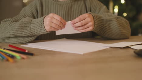 close up view of a girl in green sweater folding a letter and inserting it in a envelope sitting at a table, then gets up from the chair and leaves the room