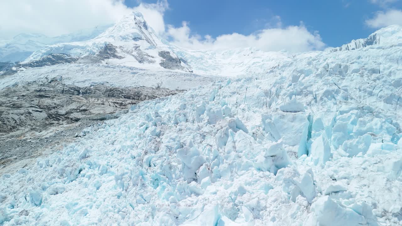 A stunning aerial drone shot flies over the vast, heavily crevassed surface of a majestic glacier in Peru's Cordillera Blanca mountain range, part of the high Andes