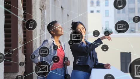 Animation-of-network-of-digital-icons-against-two-diverse-women-enjoying-the-view-from-balcony