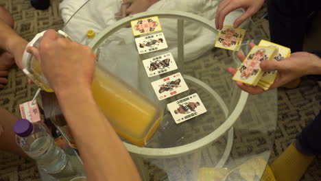 a group of friends playing cards in hong kong while drinking juice on a glass table