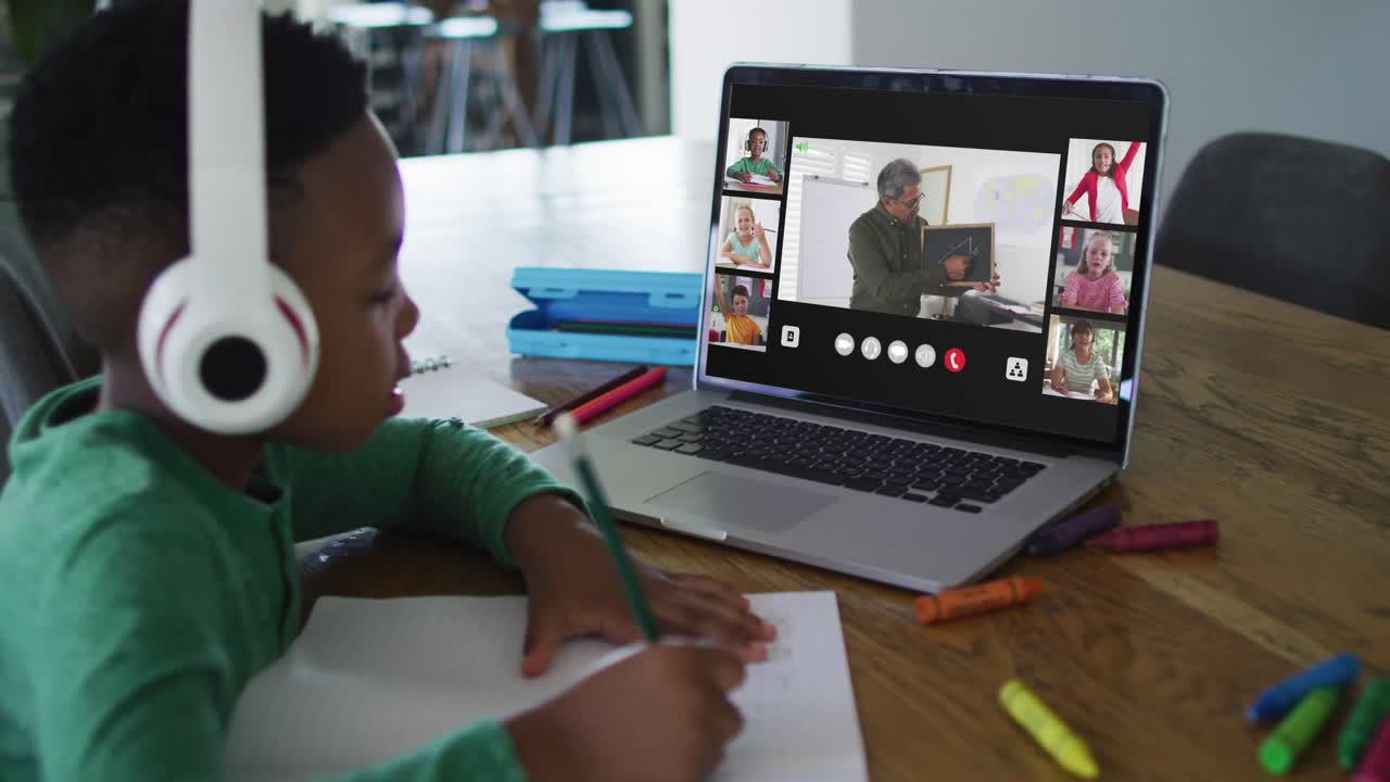 Schoolboy using laptop for online lesson at home, with diverse teacher and class on screen