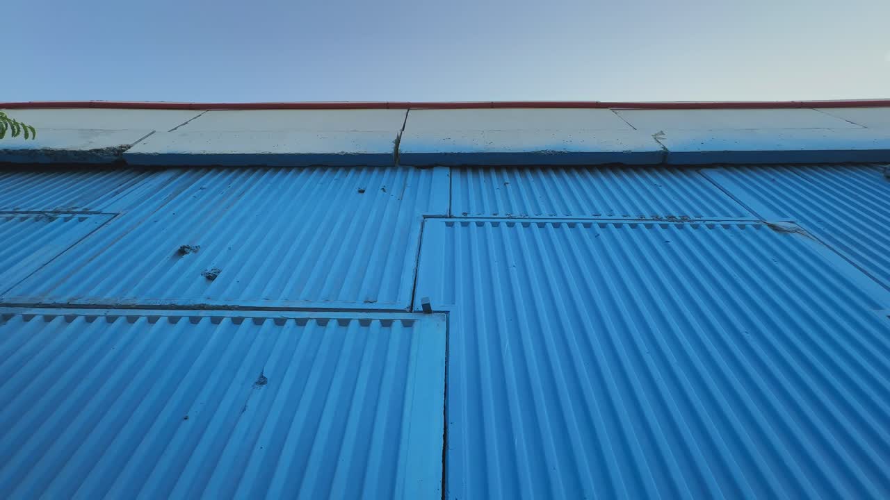 Tilt-up shot revealing the height and texture of a blue-painted concrete overbridge wall under clear morning light, emphasizing structure and perspective