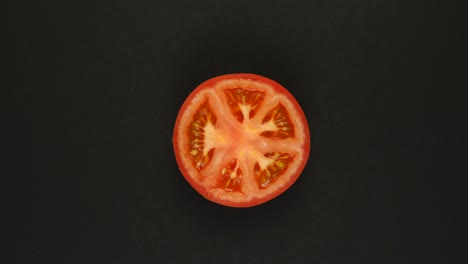 tomate giratorio sobre un fondo negro. jugos frescos, verduras, vitaminas y concepto de verano. vista superior de la mitad de un tomate jugoso