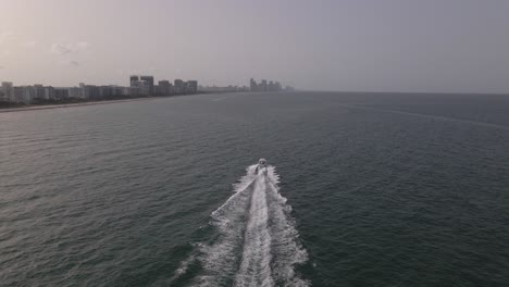 Misty-evening-aerial-tracks-motorboat-off-buildings-at-Surfside-beach