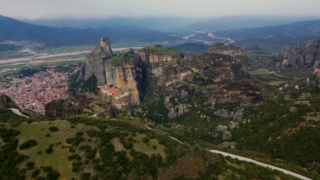 Drone circles Meteoron Monastery on cliff with distant valley and trees in Meteora, Greece