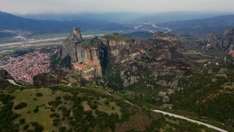 drone circles meteoron monastery on cliff with distant valley and trees in meteora, greece