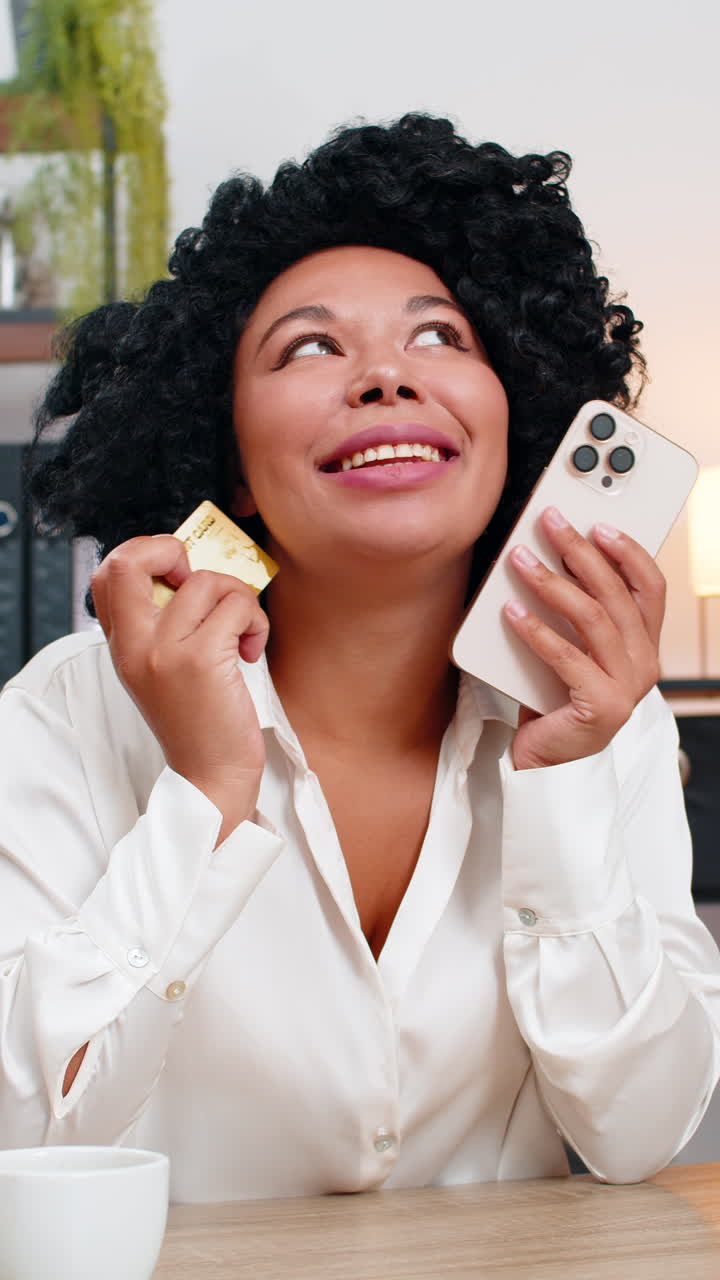 African american businesswoman smiles holding smartphone and credit card completes online purchase