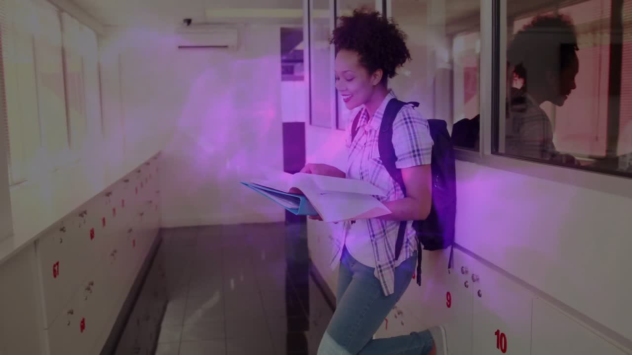Education student leaning on lockers opening textbook and reading while smiling at funny passage