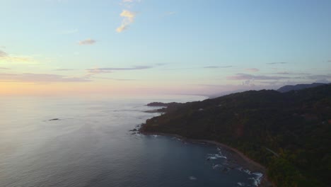 Epic-slow-forward-drone-aerial-over-trees-and-coastline-sunset-orange-blue-skies