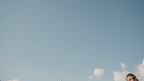 upward view of people practicing volleyball under clear sky, focus on volleyball in motion as players are engaged in a training session outdoors with bright blue sky and clouds in background