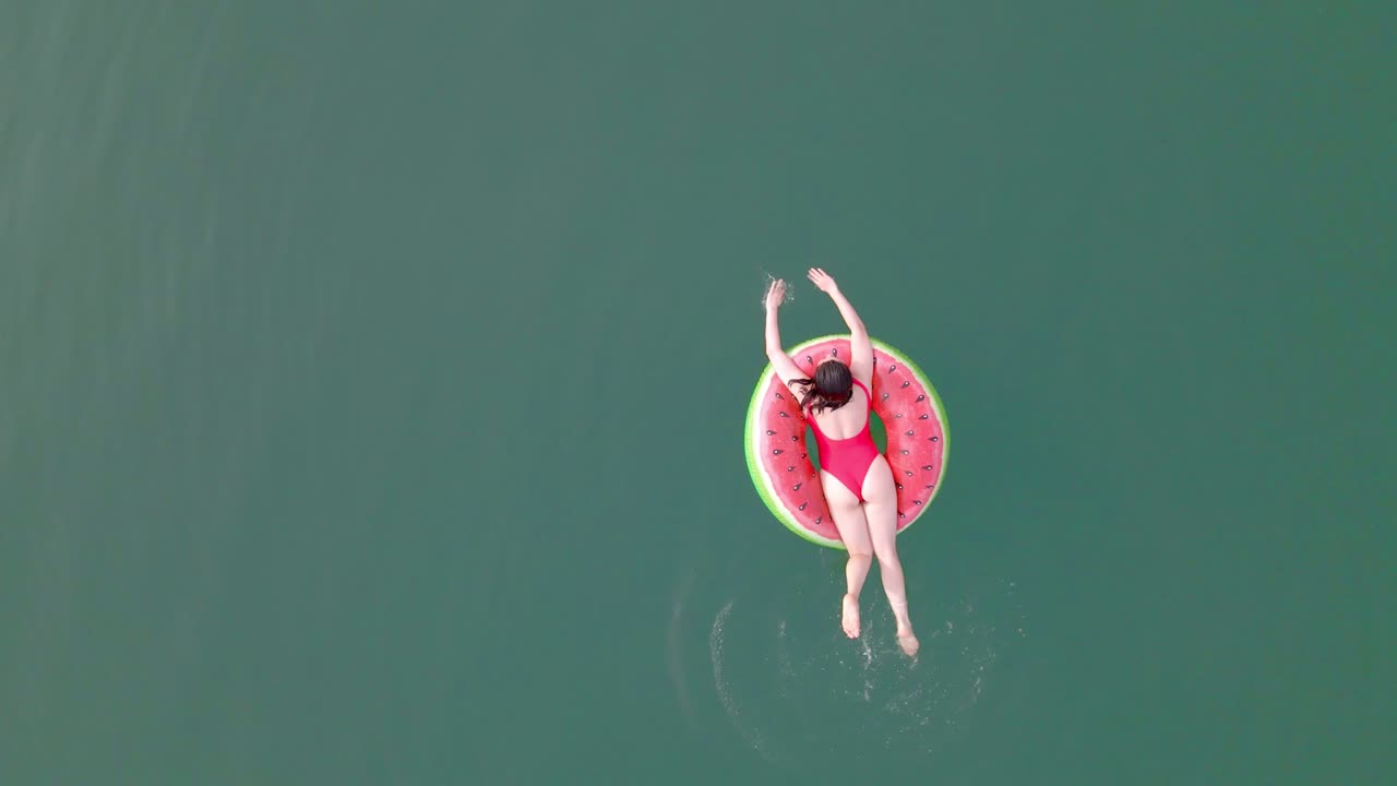 overhead top view of woman swimming with watermelon swimming circle in blue water