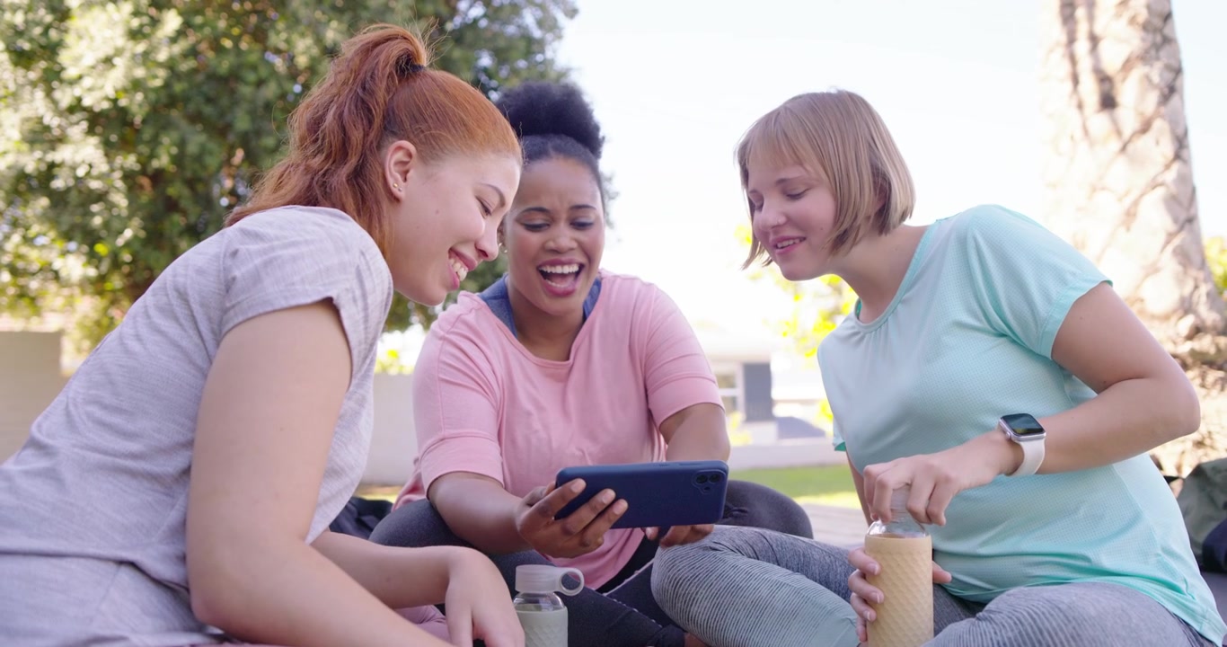 Diverse female friends reacting to tablet, rotating screen, pointing, stirring bottle on lawn