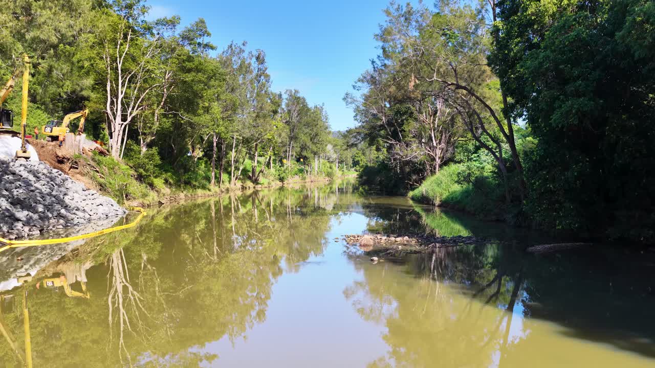 A serene stream flows through a vibrant forest in Uki, NSW, under clear blue skies, captured in natural lighting