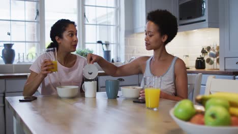mixed race lesbian couple preparing and eating breakfast in kitchen
