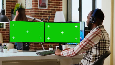 African-american-man-working-from-home-with-green-screen-on-his-display