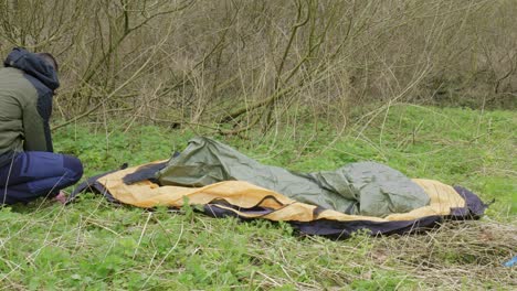 poniendo las clavijas en cada esquina de la tienda para mantenerla en su lugar, el hombre está asegurando su refugio temporal en un campamento en el bosque de thetford en brandon, reino unido.