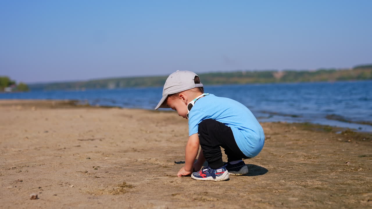 Caucasian toddler picks some sand from the beach. Child goes up to water and throws the sand into the river.