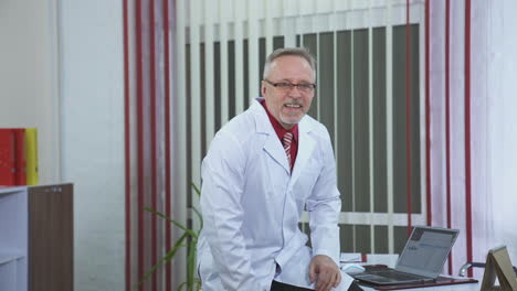smiling doctor sitting at his desk in his office. doctor is working in his medical office