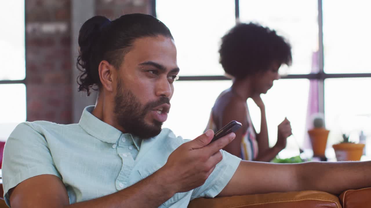Happy mixed race man sitting in cafe talking on smartphone and smiling