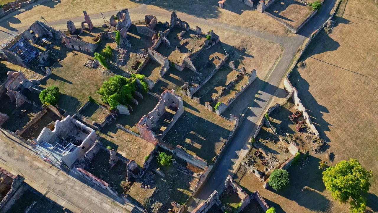 Aerial top-down drone shot of the ruins of Oradour-sur-Glane, filmed at sunset, showing destroyed buildings and streets.