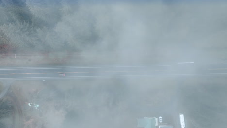 lonely red car rides by the road passing through the forest. drone footage above the highway covered with fog.
