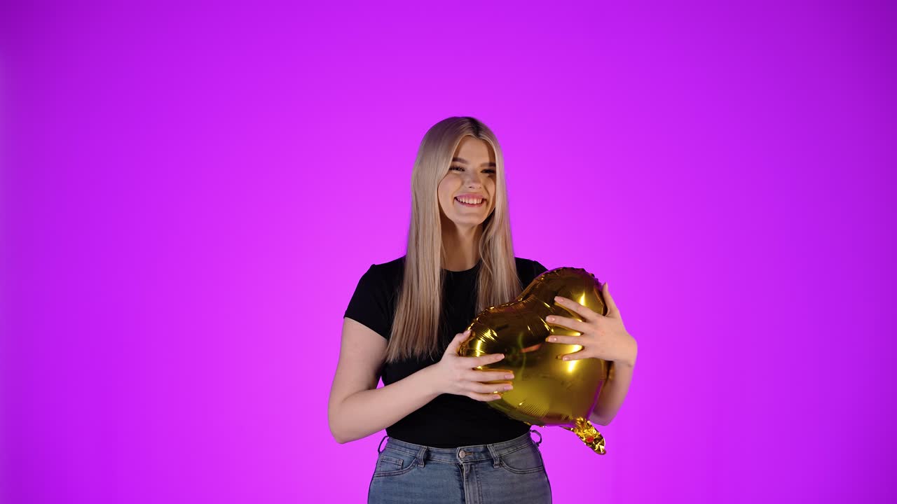Donna attraente innamorata abbraccia un palloncino a forma di cuore dorato, sorriso felice, scatto in studio