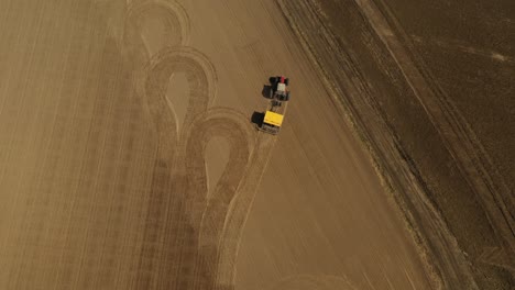 seguimiento de la vista aérea de un tractor rojo de dos ruedas con una sembradora amarilla que terminó de sembrar semillas y estacionó el tractor entre dos campos agrícolas