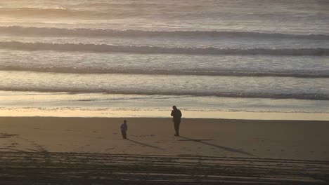 Ein-Mann-Raucht-An-Einem-Einsamen-Strand-Eine-Zigarette,-Während-Ein-Kleiner-Junge-Und-Ein-Mädchen-Um-Ihn-Herum-Spielen