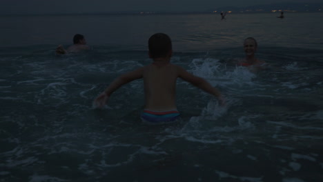 family with child bathing in sea at twilight