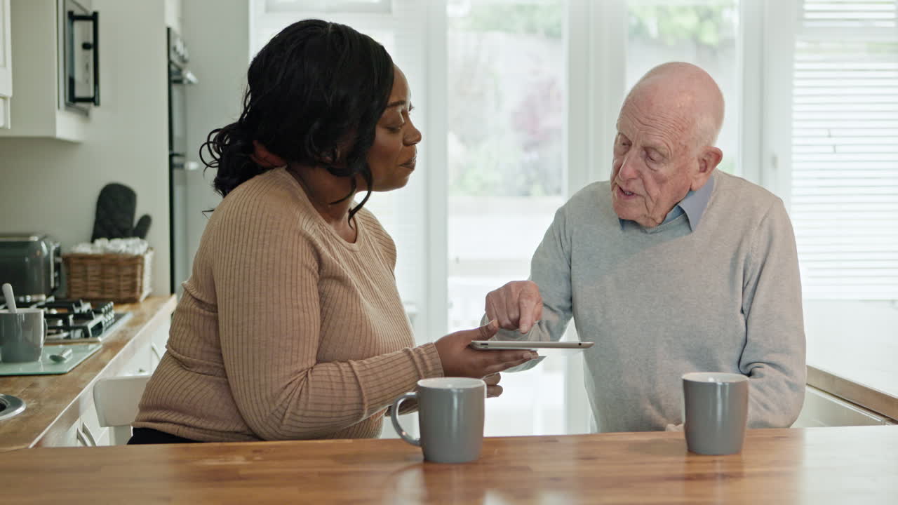 Caregiver helping senior man with tablet in kitchen