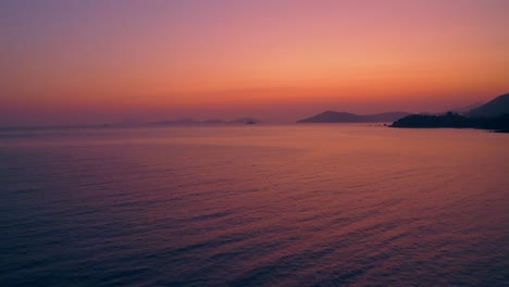 beautiful-drone-shot-of-a-natural-coastline-during-sunset,-the-light-is-clear,-red,-purple-and-gold-and-the-sea-is-reflecting-those-colors