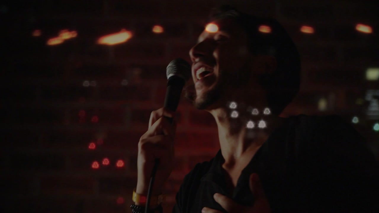 Male performer bringing mic to mouth performing music to engage crowd, bokeh lights over brick wall