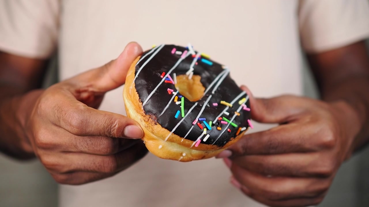 Renkli şekerlemeli, çikolata soslu donut tutan kişi.
