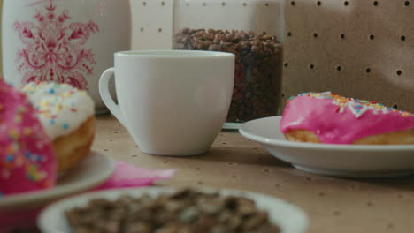 Close-up-of-person-pouring-hot-water-into-a-cup-in-breakfast-table-with-donuts