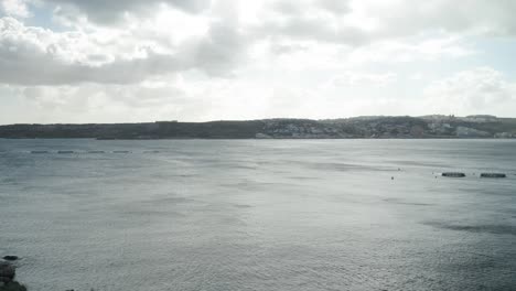 aerial: gloomy and cloudy day in mellieha bay with fish farm cages placed in water