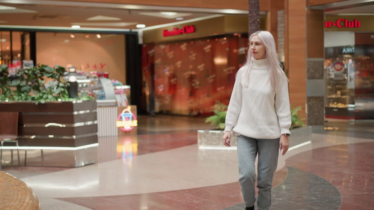 Full length women walking to indoor fountain seating area in modern shopping mall interior under bright ceiling lights with plants glass railings tile floor ambient atmosphere calm tranquil vibe