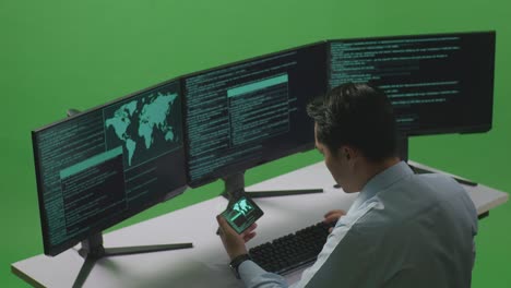 side view of asian man developer working with mobile phone while write code with multiple computer screens in green screen studio