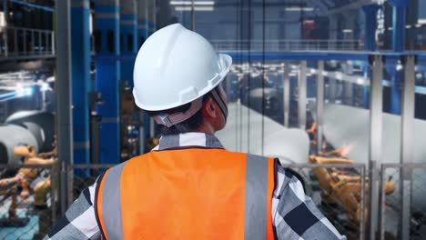 close up back view of asian male engineer with safety helmet in factory manufacture of wind turbines. standing with arms akimbo looking around, checking