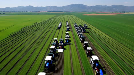 aerial view of multiple tractors working in a large green field