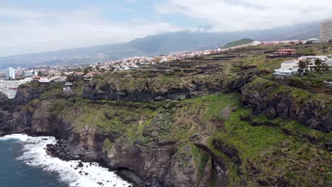 Drone-aerial-view-of-an-epic-steep-coastline-with-villages-and-houses-next-to-the-drop-in-northern-Tenerife,-Canary-Islands,-Spain