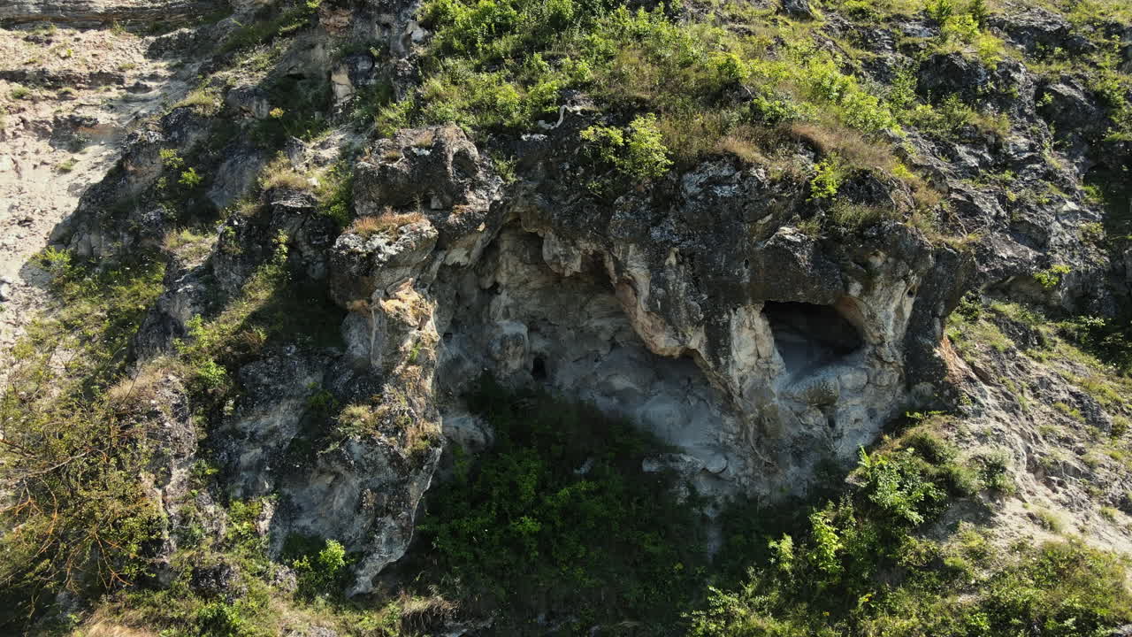 Aerial drone view of a cave in a hill slope, greenery, valley in Moldova