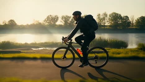 man cycling on a road beside a scenic river at sunrise or sunset