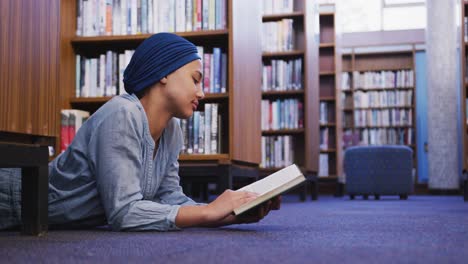 estudiante asiática vestida con un hijab azul acostada en el suelo y leyendo un libro