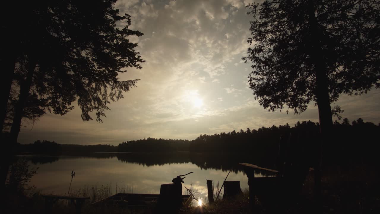 time lapse of a lake in Ontario cottage country with the silhouette of trees and reflection on the lake, while clouds roll past in the summer. Canada