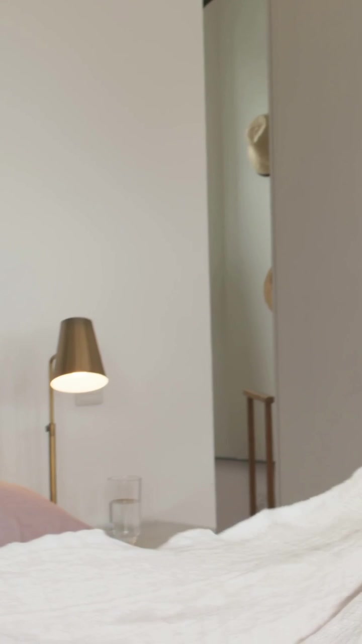 Vertical video: Entering man with cover laying bed in bedroom woman smoothing with cloth making bed